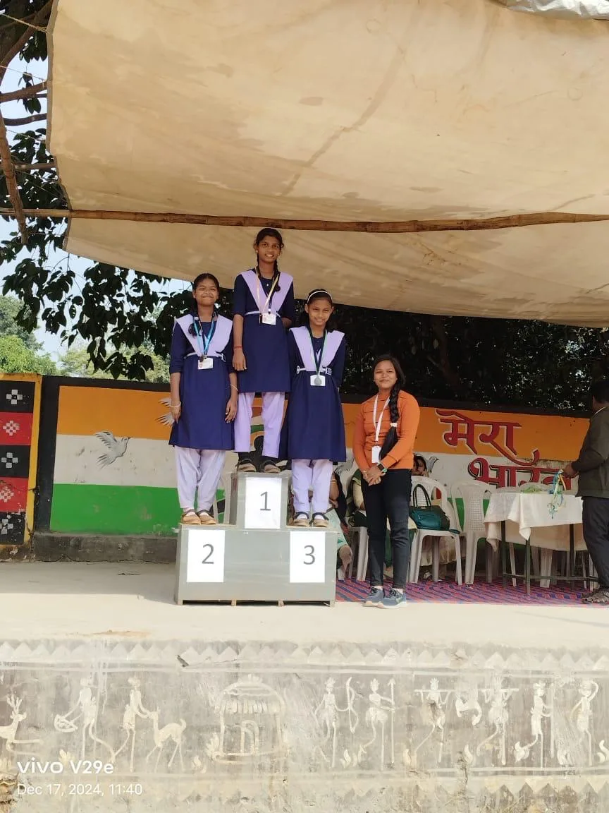 Students standing on a podium with a teacher during a prize distribution.